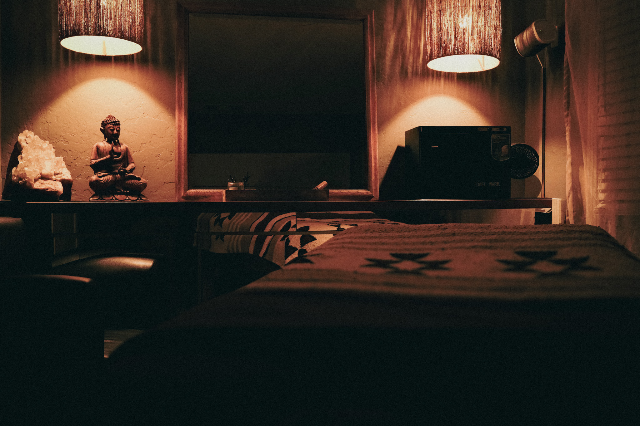 A current Almonte Spa treatment room with warm light, a Buddha, crystal, and massage table