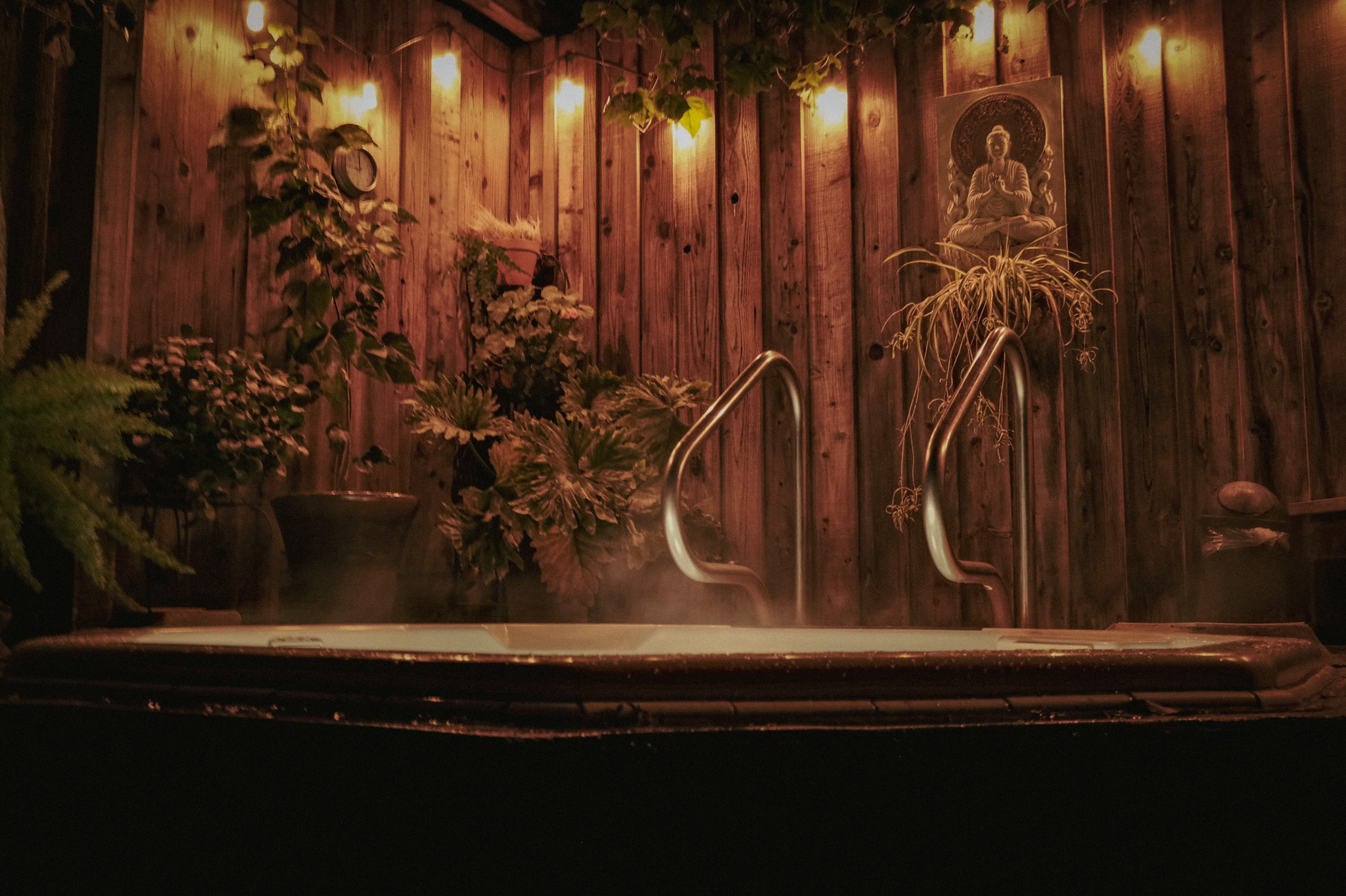 Steam rising from a private outdoor hot tub beneath warm lights, cedar, and trailing plants